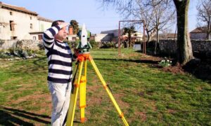 Surveyor conducting a property survey with tripod equipment in a residential yard