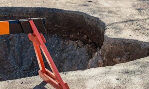 A sinkhole in a residential street marked with a barrier showing why a due diligence survey is essential before building