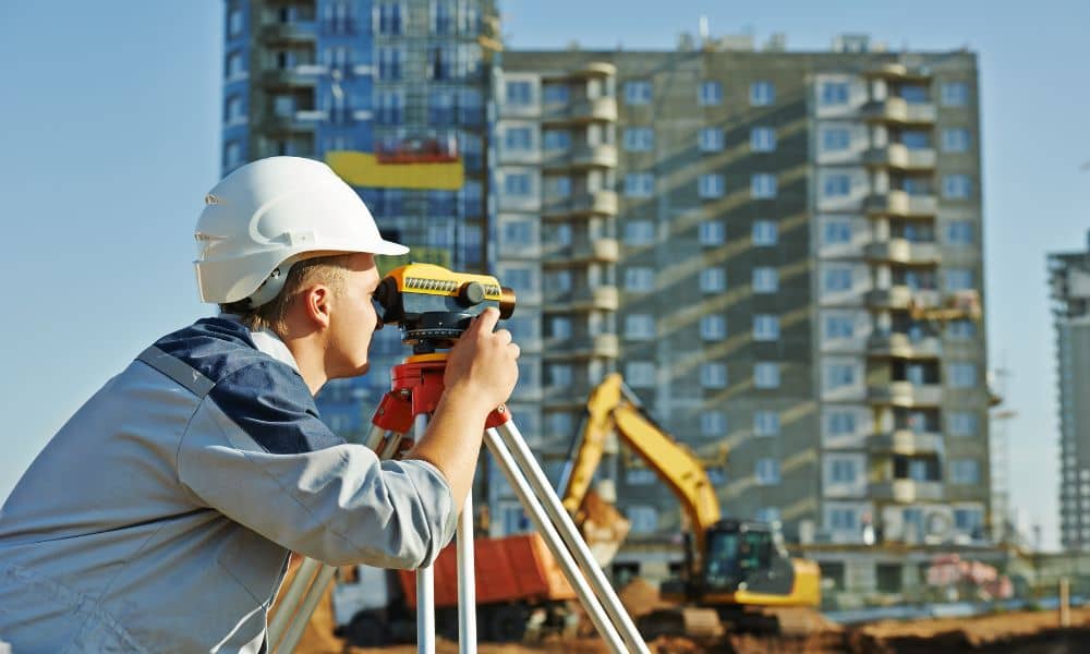 Surveyor using a total station for an alta land title survey at an urban construction site with buildings in the background