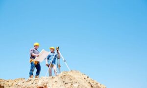 Surveyors using equipment on a sloped site to record data for an ALTA survey and assess ground stability under new landslide insurance standards