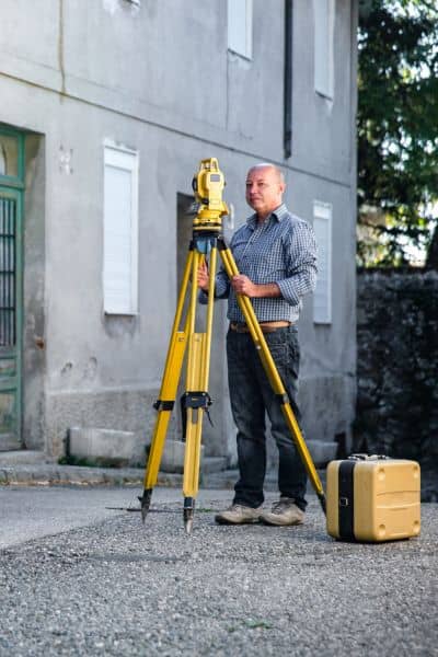 Licensed land surveyor measuring property elevations with total station for updated elevation certificate
