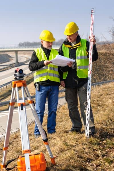 Two land surveyors reviewing site plans with equipment, showing how a due diligence survey ensures safe development

