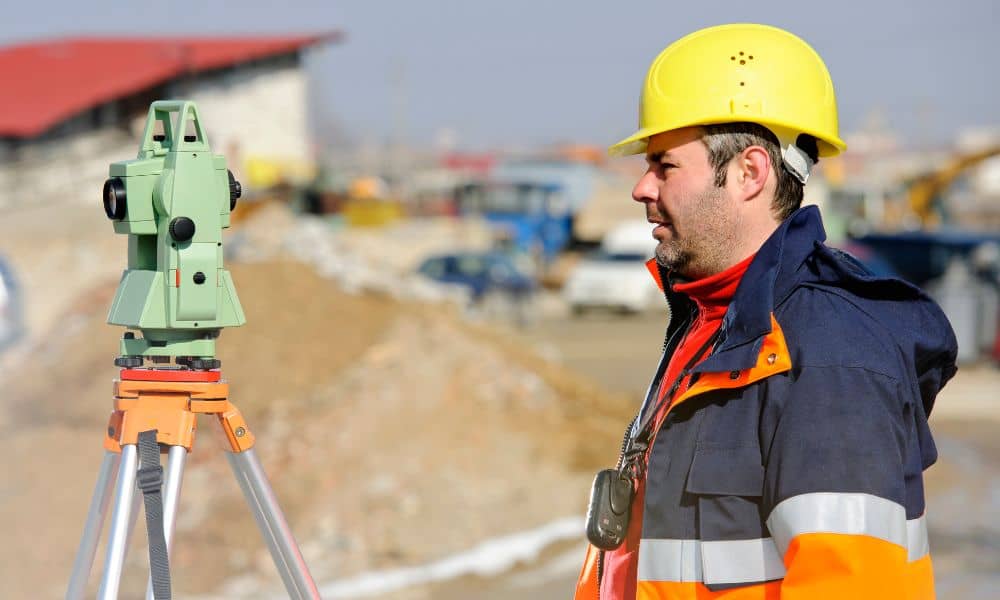 Licensed land surveyor using a total station to perform a boundary line survey on an active construction site