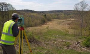 A land surveyor works on vacant rural property near Pittsburgh, showing the terrain that can affect the average cost for a land survey
